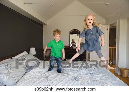 Stock Image - Girl and brother jumping on bed together. Fotosearch