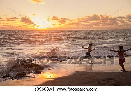 Stock Image - Girl and brother running on beach at sunrise, Blowing Rocks Preserve, Jupiter Island, Florida, USA. Fotosearch