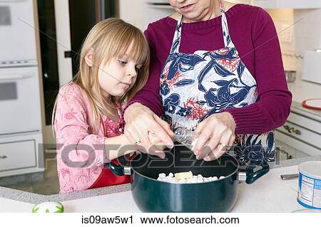 Stock Image - Girl and grandmother measuring salt for saucepan. Fotosearch