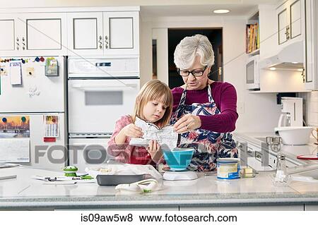 Stock Photo - Girl and grandmother pouring cake mix at kitchen counter. Fotosearch
