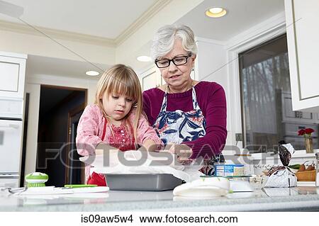 Picture - Girl and grandmother preparing greaseproof paper at kitchen counter. Fotosearch