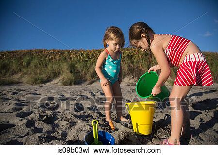 Stock Image - Girl and sister playing with toy buckets on beach, Blowing Rocks Preserve, Jupiter Island, Florida, USA. Fotosearch