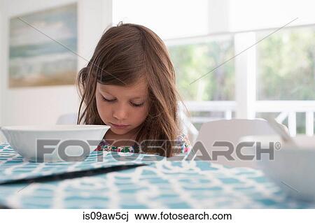 Stock Image - Girl at dining table looking down. Fotosearch