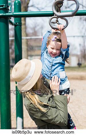 Girl hanging on climbing frame in mother's arms View Large Photo Image Stock Photograph - Girl hanging on climbing frame in mother's arms. Fotosearch