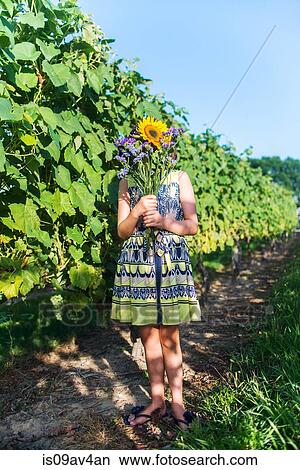 Picture - Girl holding bunch of flowers in front of face in vineyard. Fotosearch