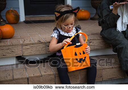 Girl in cat costume peering into trick or treating bag on porch stairway View Large Photo Image Stock Image - Girl in cat costume peering into trick or treating bag on porch stairway. Fotosearch