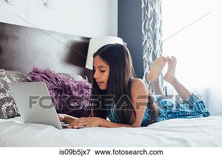 Girl lying on bed using laptop View Large Photo Image Stock Photo - Girl lying on bed using laptop. Fotosearch