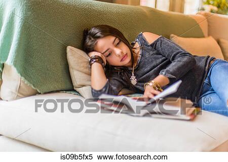 Stock Photography - Girl lying on sofa reading book. Fotosearch