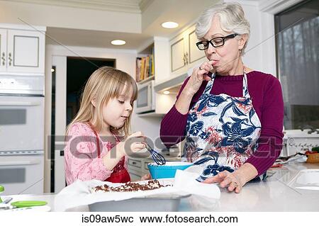 Girl mixing cake at kitchen counter whilst grandmother licking her fingers View Large Photo Image Stock Image - Girl mixing cake at kitchen counter whilst grandmother licking her fingers. Fotosearch