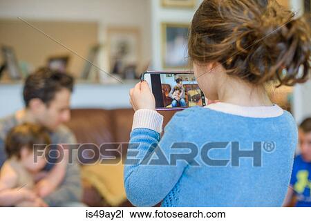Stock Image - Girl photographing family in living room. Fotosearch