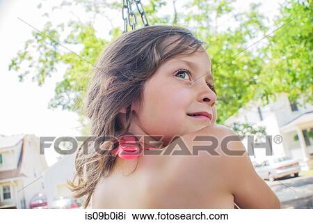 Stock Image - Girl playing on swing in garden looking over her shoulder. Fotosearch