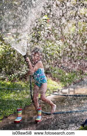 Stock Photo - Girl playing with water hose on sidewalk. Fotosearch