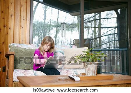Girl sitting on living room sofa using touchscreen on digital tablet View Large Photo Image Stock Image - Girl sitting on living room sofa using touchscreen on digital tablet. Fotosearch