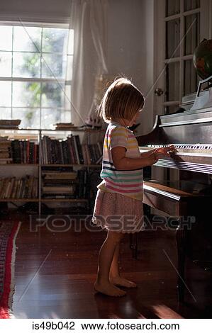 Stock Image - Girl standing playing old piano at home. Fotosearch