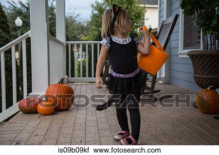 Stock Image - Girl trick or treating in cat costume looking over her shoulder on porch. Fotosearch