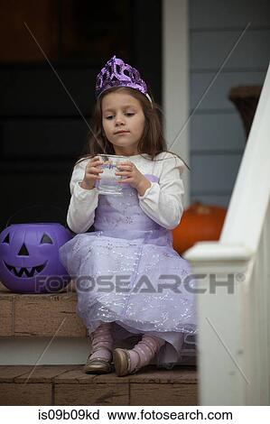 Stock Image - Girl trick or treating in fairy costume sitting on stairway drinking lemonade. Fotosearch