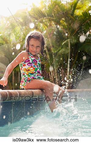 Girl wearing swimming costume sitting on sunlit poolside splashing View Large Photo Image Stock Photo - Girl wearing swimming costume sitting on sunlit poolside splashing. Fotosearch