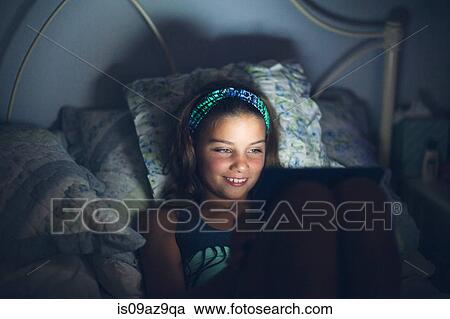 Stock Image - Girls in bed using digital tablet smiling. Fotosearch