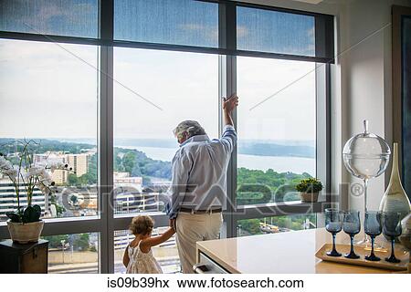 Grandfather holding granddaughter's hand looking out of window at home View Large Photo Image Stock Photo - Grandfather holding granddaughter's hand looking out of window at home. Fotosearch