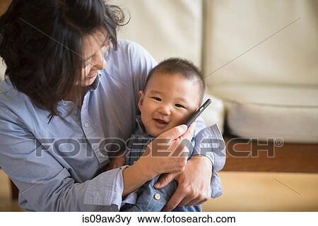 Grandmother holding smartphone to grandson's ear View Large Photo Image Stock Photo - Grandmother holding smartphone to grandson's ear. Fotosearch