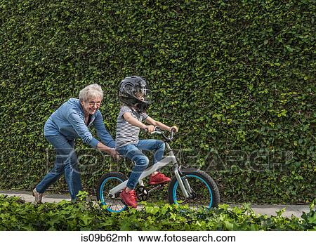 Stock Image - Grandmother pushing grandson on his bicycle. Fotosearch