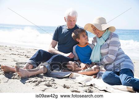 Stock Image - Grandparents and grandson, sitting on beach, smiling. Fotosearch