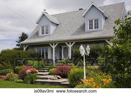 Stock Image - Grey brick with white trim cottage style Canadiana home facade with landscaped front yard in summer. Fotosearch