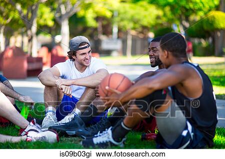 Stock Image - Group of male friends sitting together in park, laughing. Fotosearch