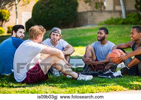Stock Image - Group of male friends sitting together in park, laughing. Fotosearch