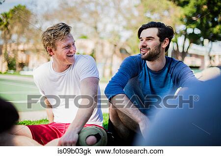 Stock Image - Group of male friends sitting together in park, laughing. Fotosearch