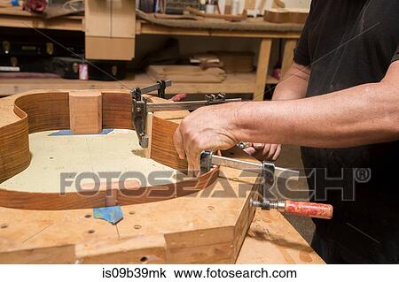 Stock Image - Guitar maker in workshop manufacturing guitar. Fotosearch