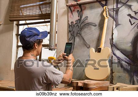 Stock Photo - Guitar maker in workshop photographing guitar. Fotosearch
