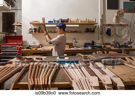 Stock Image - Guitar maker in workshop quality checking guitar neck. Fotosearch