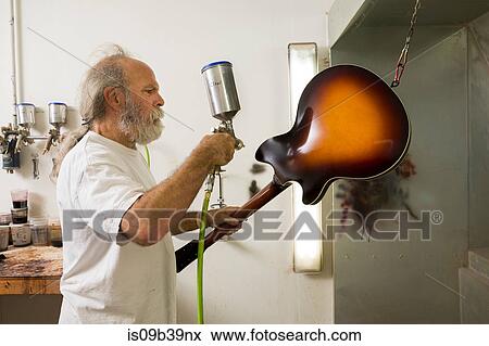 Stock Photo - Guitar maker in workshop using spray gun to varnish guitar. Fotosearch