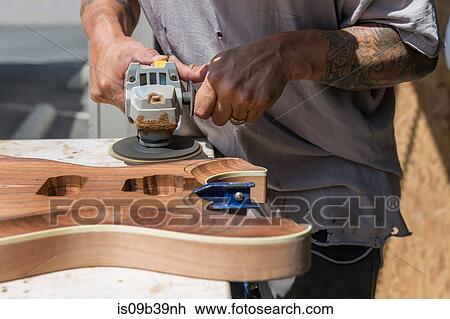 Stock Image - Guitar maker manufacturing guitar in workshop. Fotosearch