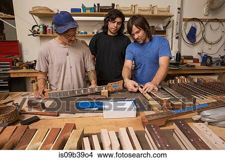 Picture - Guitar makers in workshop quality checking guitar necks. Fotosearch