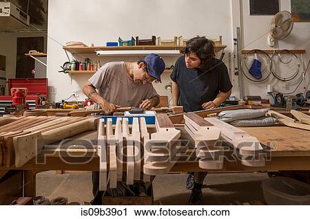 Stock Image - Guitar makers in workshop quality checking guitar necks. Fotosearch