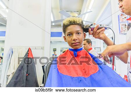 Stock Photography - Hairdresser cutting teenage boy's hair in barbershop. Fotosearch