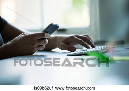 Hand of male designer using smartphone and typing on keyboard at creative studio desk View Large Photo Image Stock Image - Hand of male designer using smartphone and typing on keyboard at creative studio desk. Fotosearch