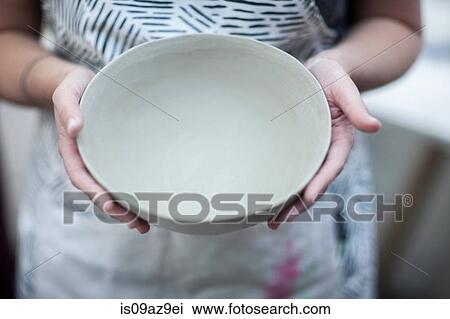 Stock Image - Hands of female potter holding finished bowl in workshop. Fotosearch