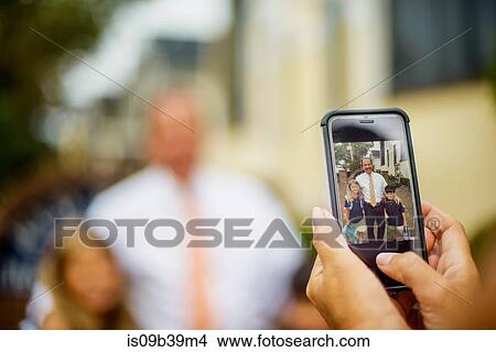 Picture - Hands of mother photographing male and female elementary school twins with father on smartphone. Fotosearch