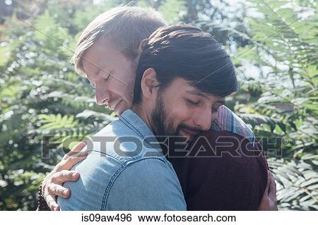 Stock Photograph - Head and shoulder view of male couple hugging in park. Fotosearch