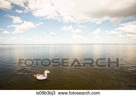 Stock Image - High angle distant view of young woman sitting on inflatable unicorn in sea, Santa Rosa Beach, Florida, USA. Fotosearch