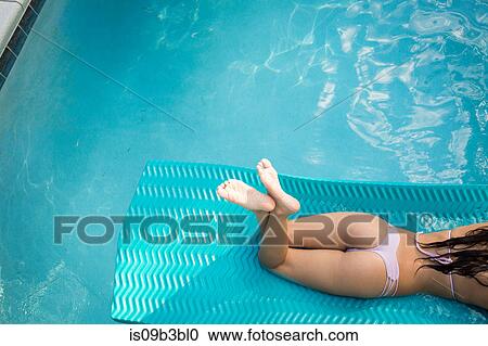 Stock Image - High angle neck down view of young woman sunbathing in swimming pool, Santa Rosa Beach, Florida, USA. Fotosearch