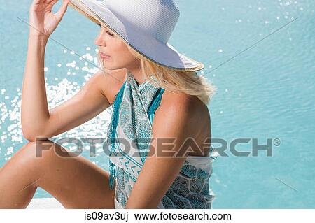 High angle side view of young woman wearing sun hat sitting by swimming pool View Large Photo Image Stock Image - High angle side view of young woman wearing sun hat sitting by swimming pool. Fotosearch