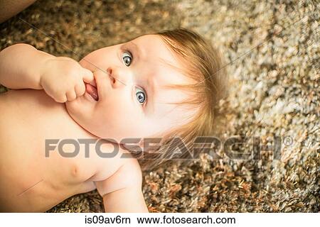 High angle view of baby girl lying on carpet, finger in mouth looking away View Large Photo Image Picture - High angle view of baby girl lying on carpet, finger in mouth looking away. Fotosearch
