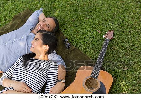 High angle view of couple lying on grass with acoustic guitar smiling View Large Photo Image Stock Image - High angle view of couple lying on grass with acoustic guitar smiling. Fotosearch