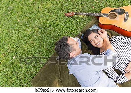 Stock Photography - High angle view of couple lying on grass with acoustic guitar smiling. Fotosearch