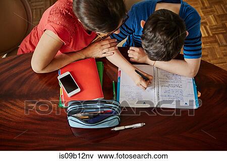 Stock Photo - High angle view of mother at dining table helping son with homework. Fotosearch