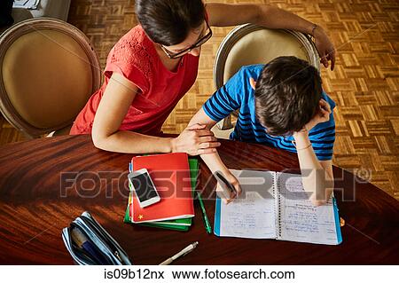 Stock Photo - High angle view of mother at dining table helping son with homework. Fotosearch
